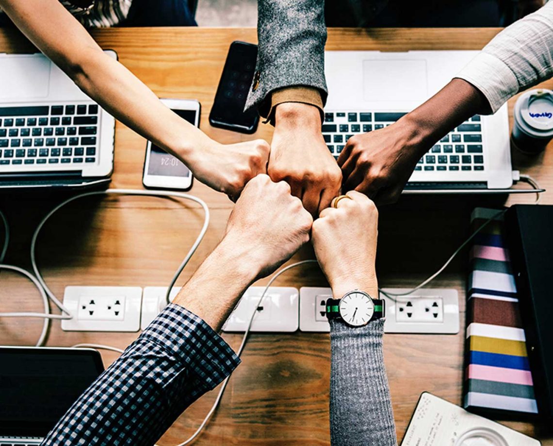 group of people fist bumping over a desk